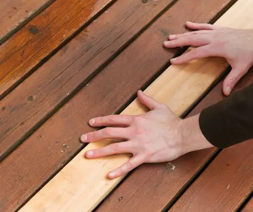 Hands fitting a new board into a stained wood deck